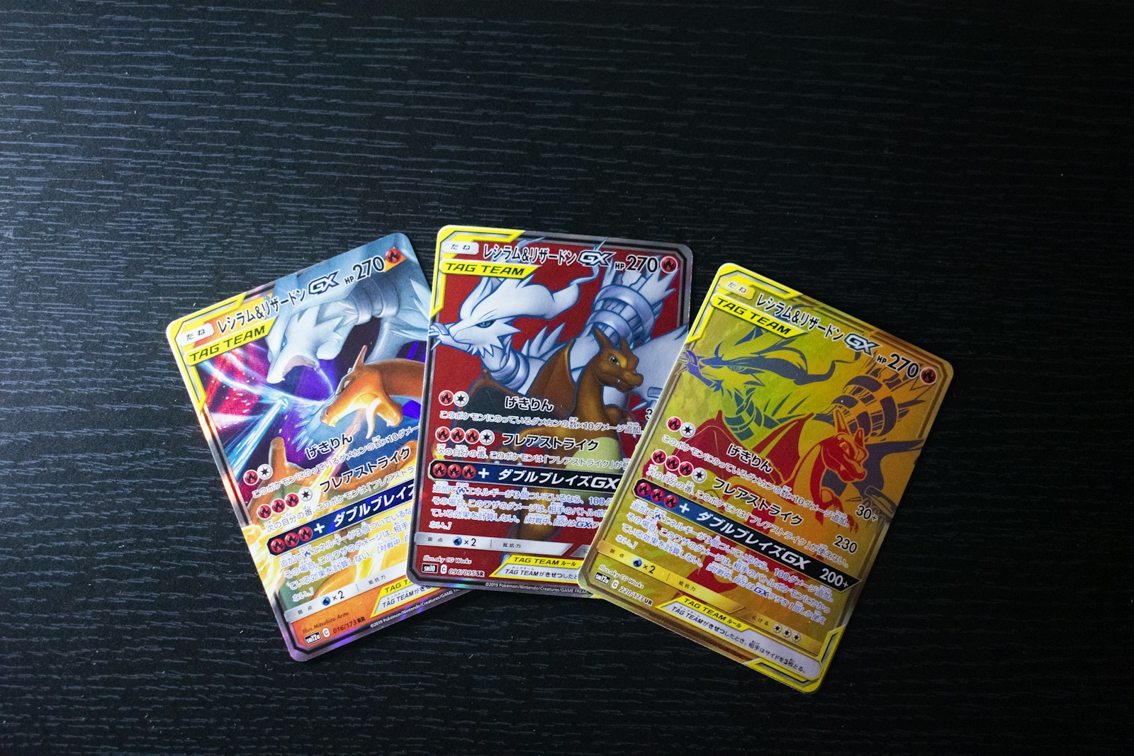 Drei japanische Reshiram und Glurak GX Karten mit unterschiedlichen Motiven auf einer dunklen Tischplatte.