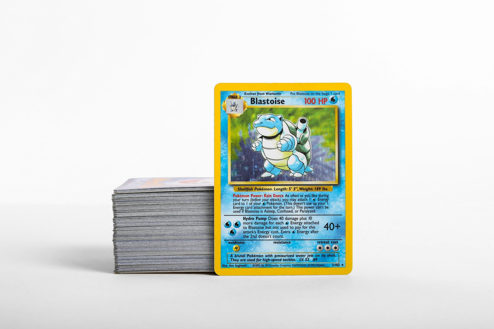 Eine Blastoise-Pokémon-Karte neben einem Stapel Sammelkarten auf einer hellen Fläche.